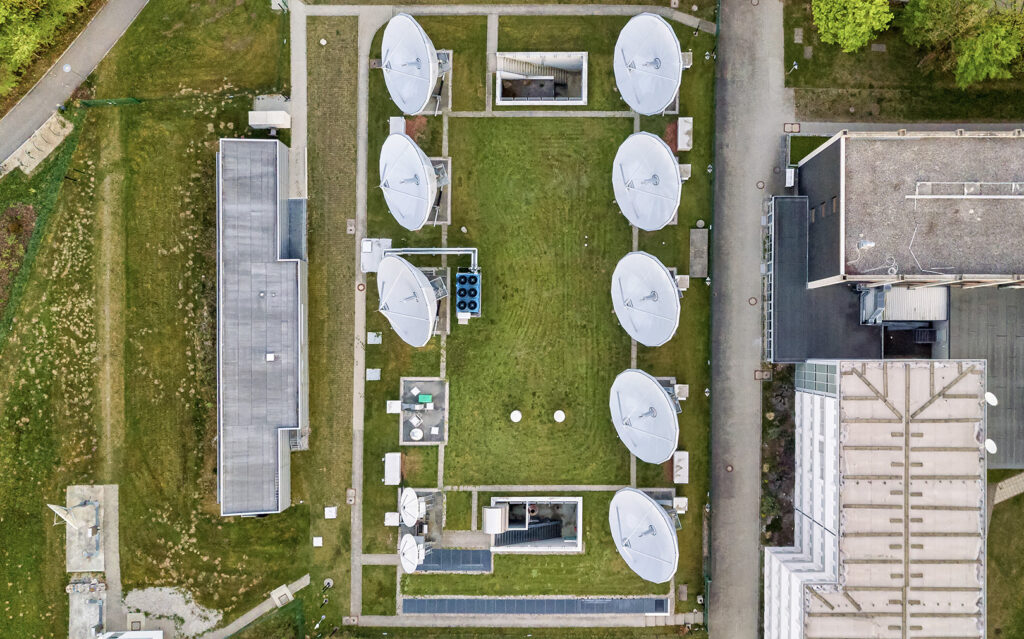 Vue aérienne d'un réseau satellitaire avec plusieurs grandes antennes paraboliques disposées en grille sur une pelouse verte.