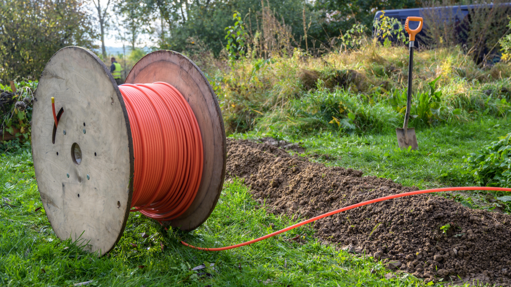 Un cable de fibra naranja en un campo junto a un agujero y una pala