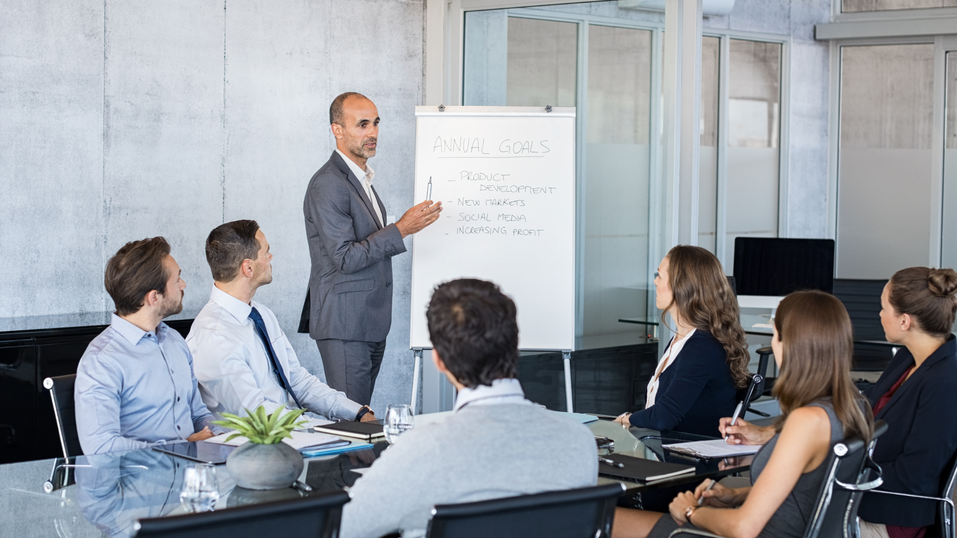 A group of business professionals is engaged in a meeting where a presenter is explaining the company's annual goals