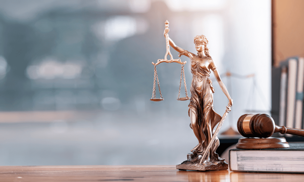 A statue of Lady Justice holding scales and a sword, placed next to a gavel on a desk, symbolizing governance and legal compliance.